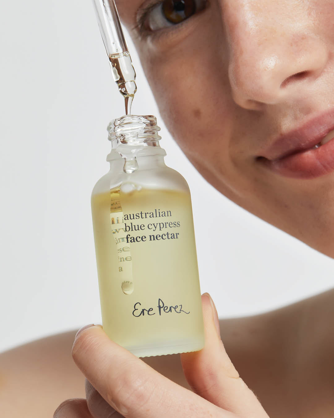 Natural Australian blue cypress face nectar by Ere Perez in its recyclable glass bottle and applied on the skin for a hydrating and brightening effect