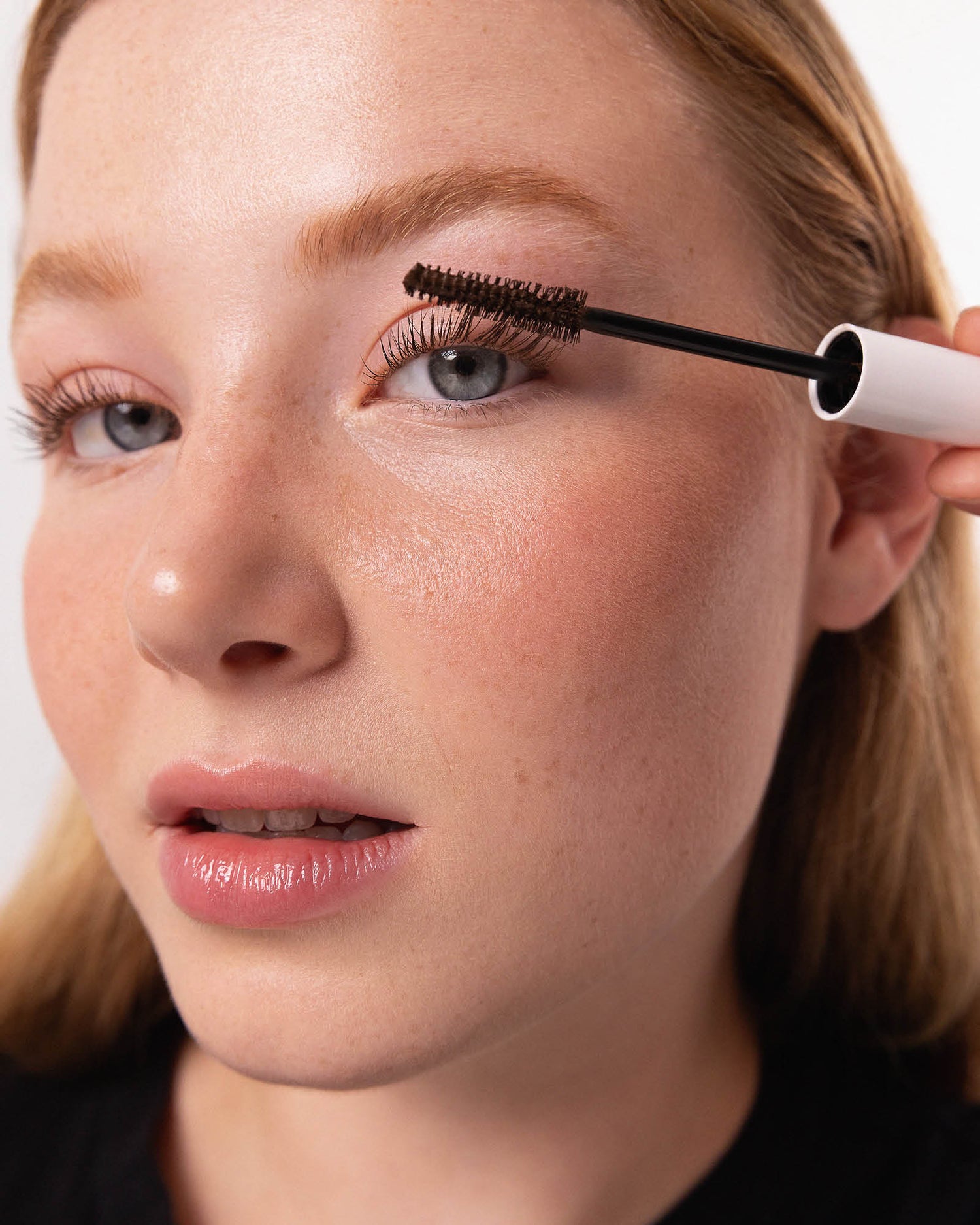 Person applying mascara to their eyelashes with a close-up view. #shade_brown