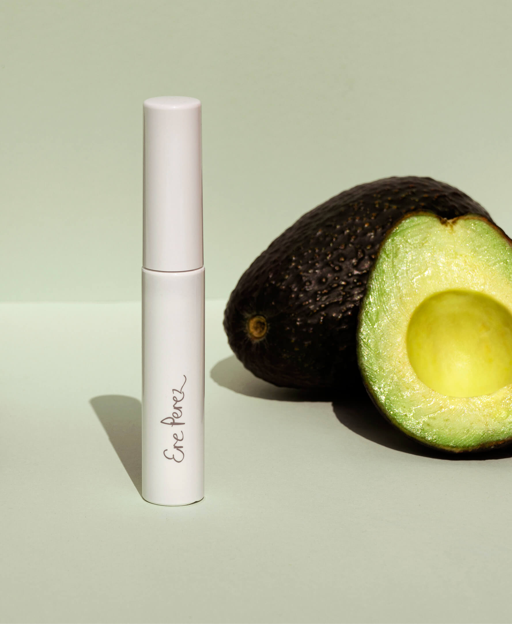 Eco-friendly and vegan avocado waterproof mascara tube by Ere Perez next to its star ingredient: avocado