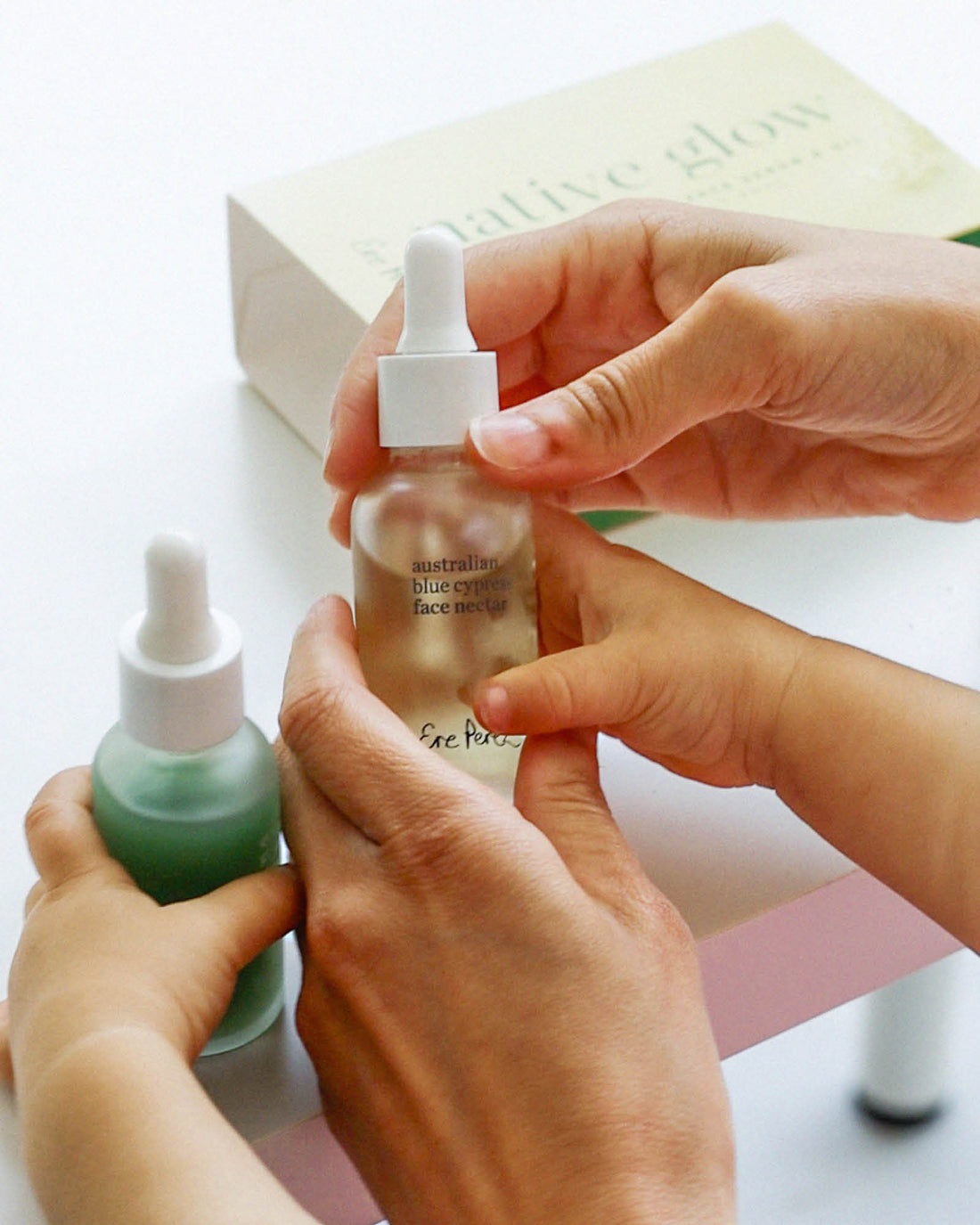 Person holding a skincare serum bottle with another bottle and a box in the background. Australian Blue Cypress Face Nectar