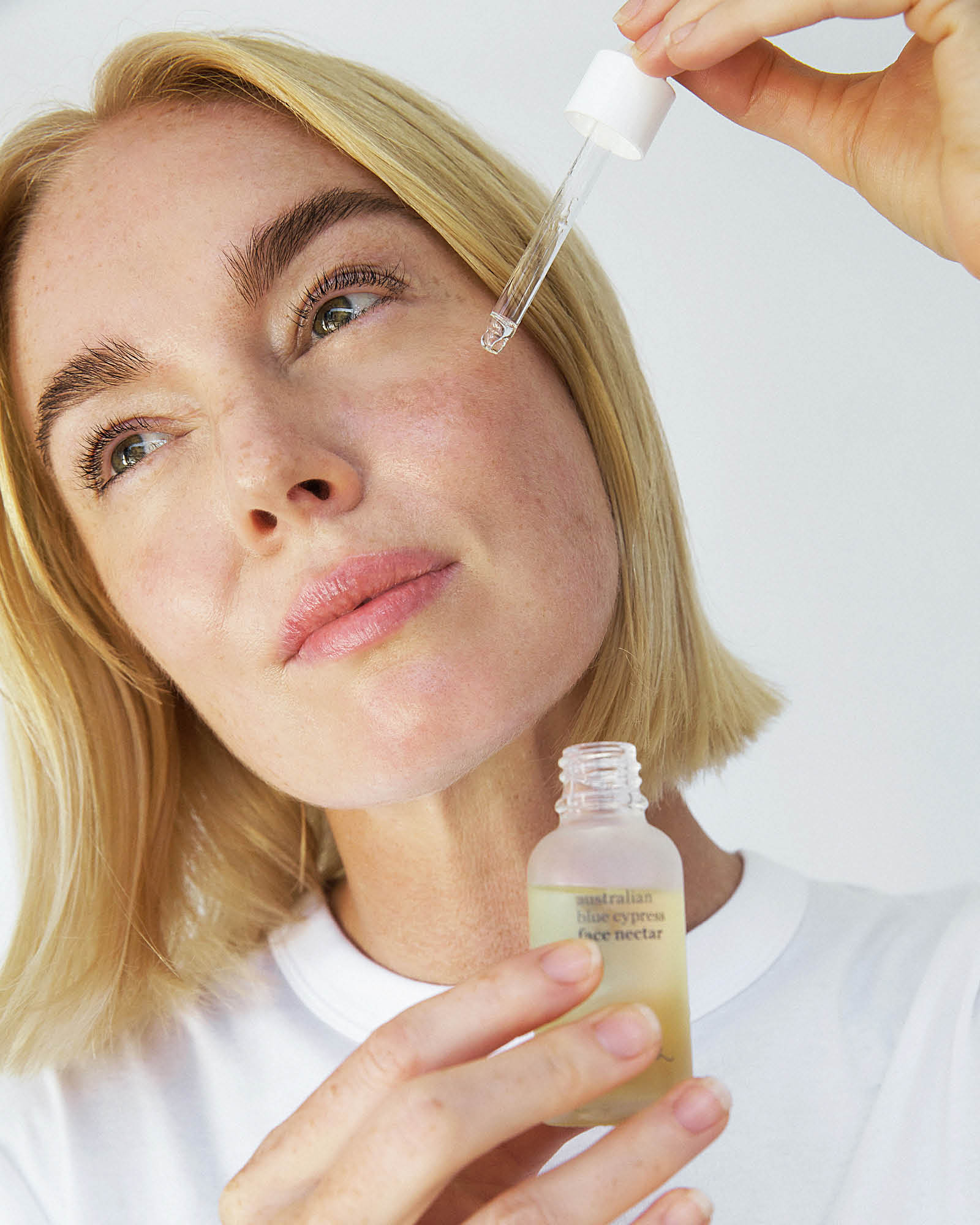 Woman holding a dropper with a skincare product and a bottle australian blue cypress face nectar