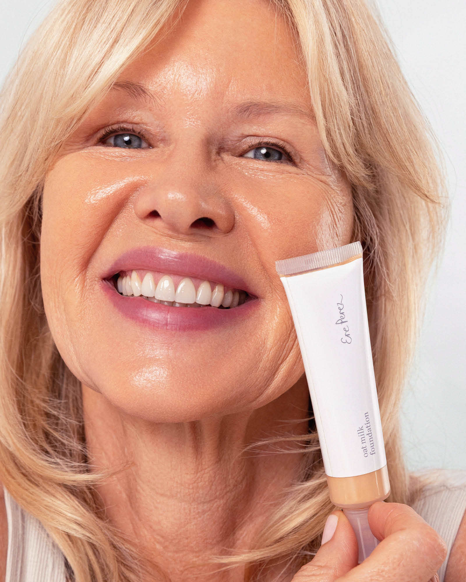 Woman applying a cosmetic product to her face with a focus on the product packaging. Oat Milk Foundation in