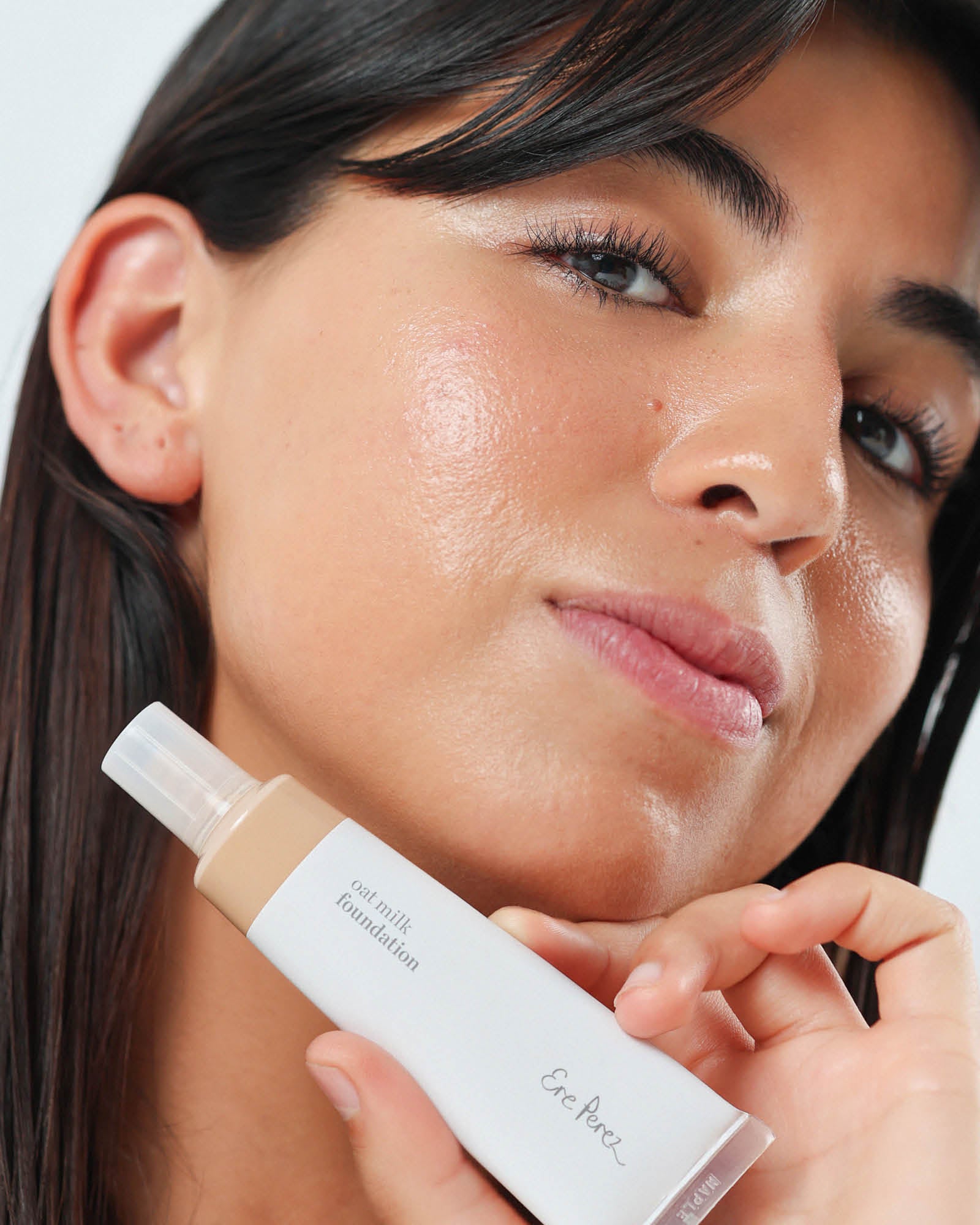 Woman holding a bottle of foundation in the shade maple close to her face,