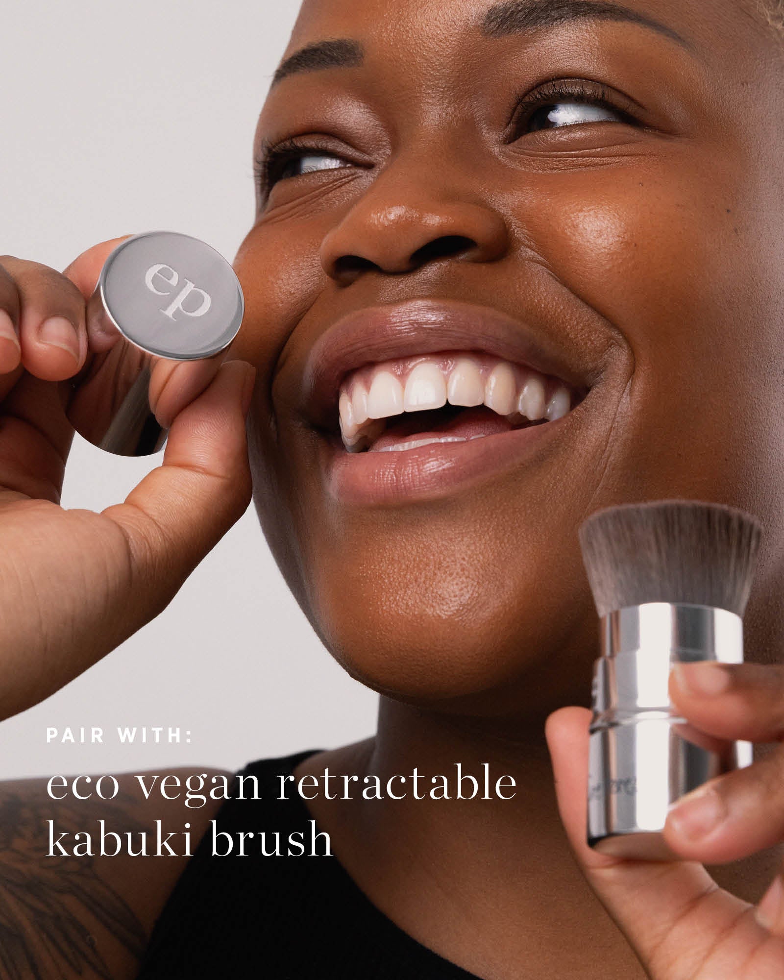 Person applying makeup with a silver makeup brush, featuring the brand &