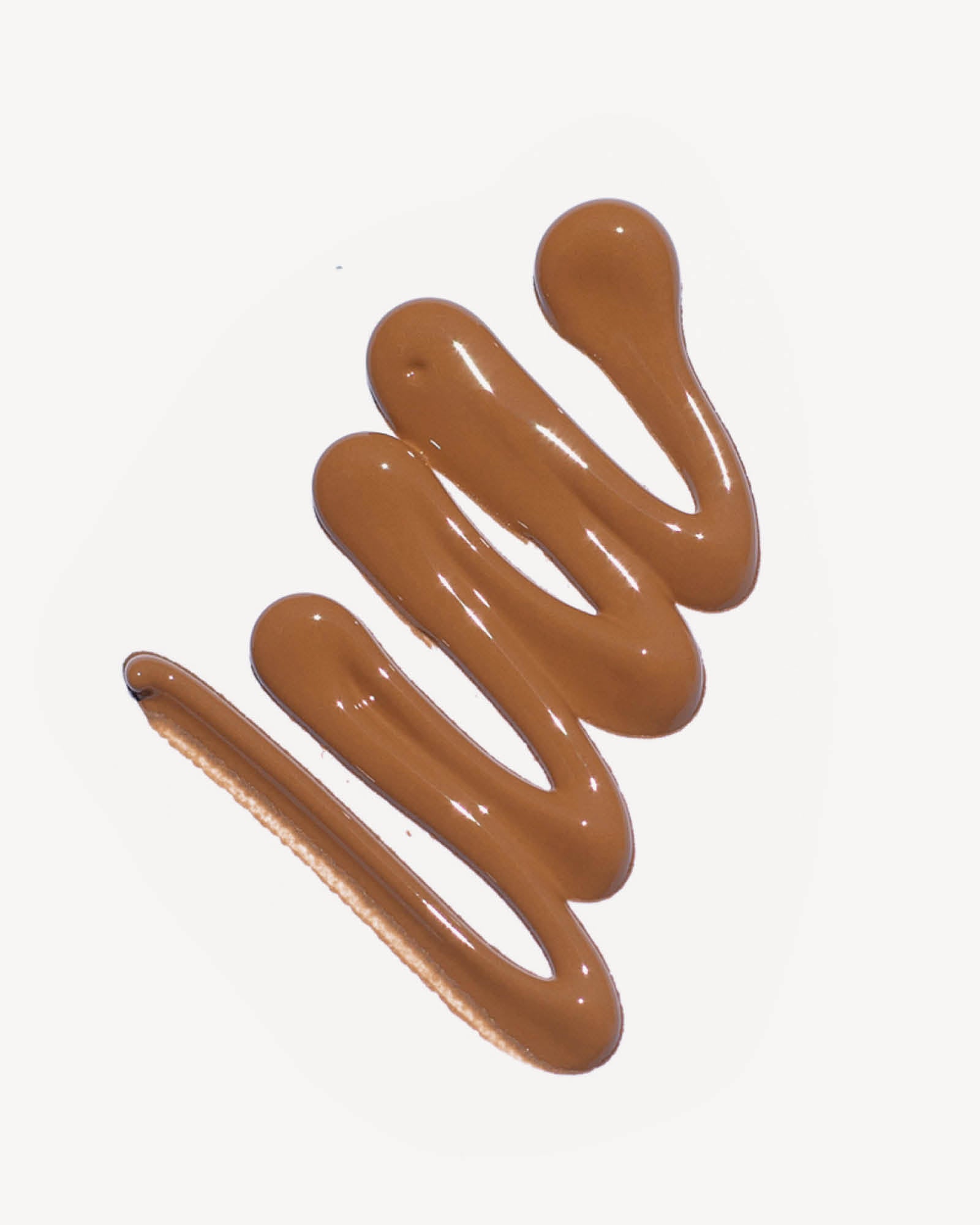 Swirls of brown liquid on a white background. Oat Milk Foundation in Shade Toffee,