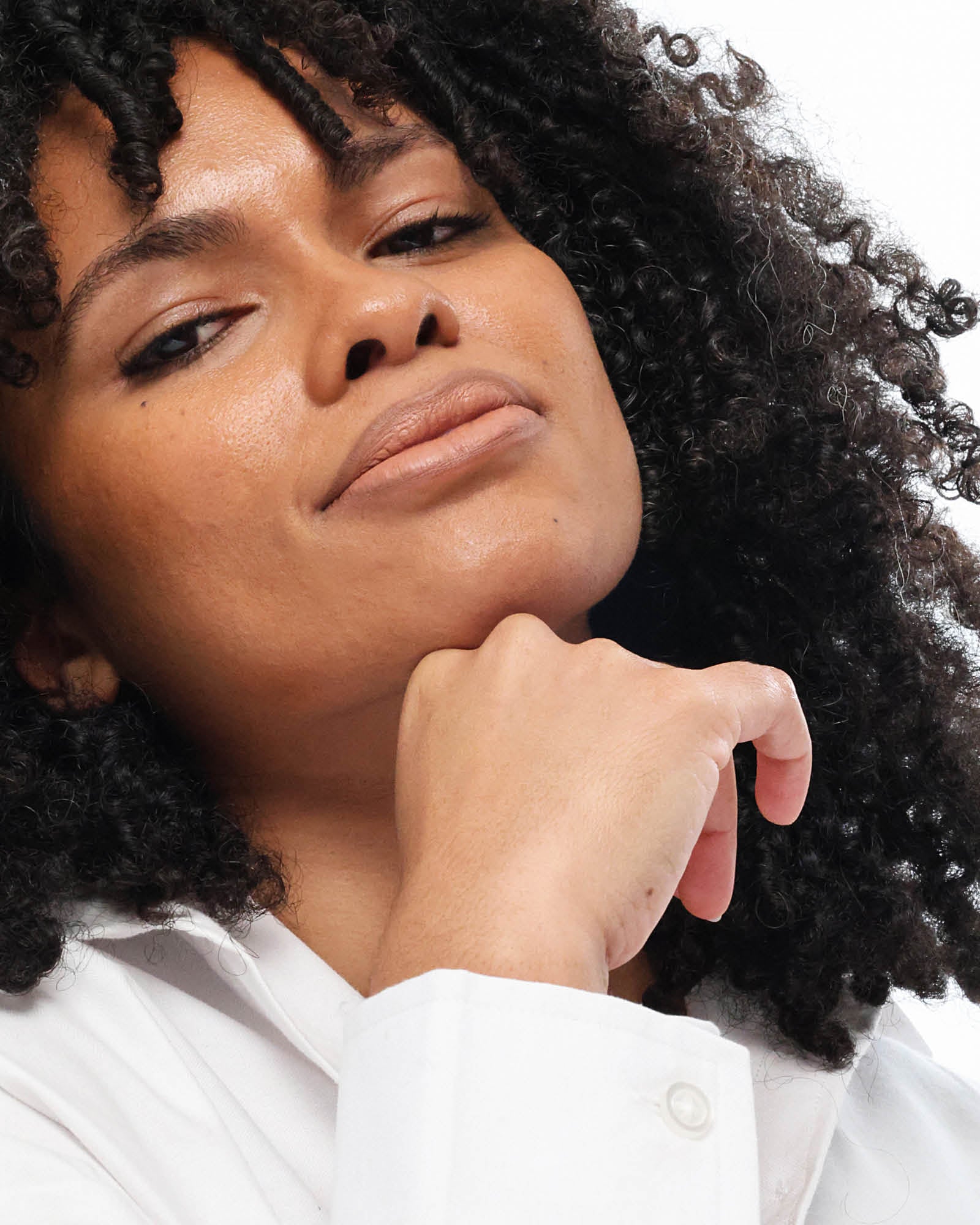 Person with curly hair wearing a white shirt against a neutral background,