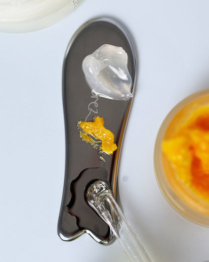 Ere Perez stainless steel face tool with product applied on it to sculpt and spread product on skin