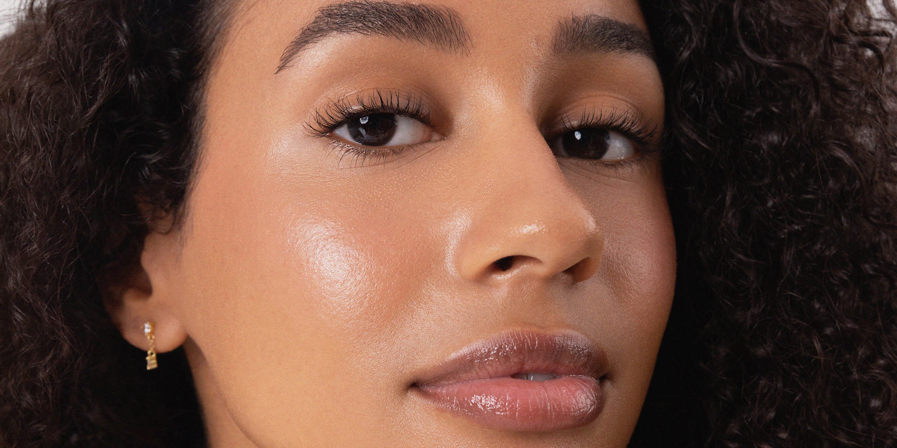 Close-up portrait of a model with glowing natural skin, soft brows and glossy lips, showcasing a fresh Ere Perez complexion look.