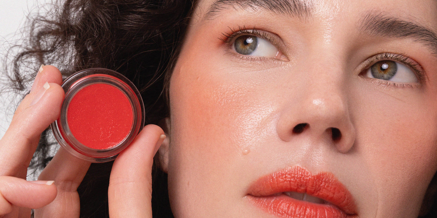 Lady holding Ere Perez carrot colour pot blush near her face 