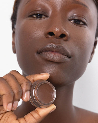 Person has applied Arnica All Cover Pot to their face with a close-up of the product. Arnica All Cover Pot in the shade espresso 