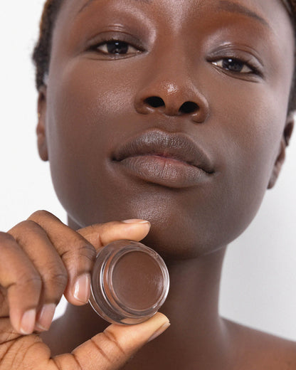 Person has applied Arnica All Cover Pot to their face with a close-up of the product. Arnica All Cover Pot in the shade espresso 