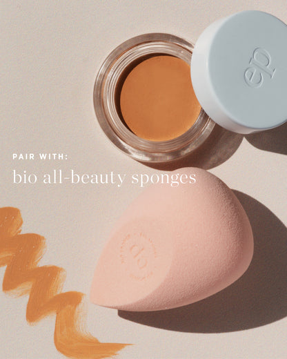 One pink beauty sponge, with makeup application strokes on a light background next to Arnica All Cover Pot 