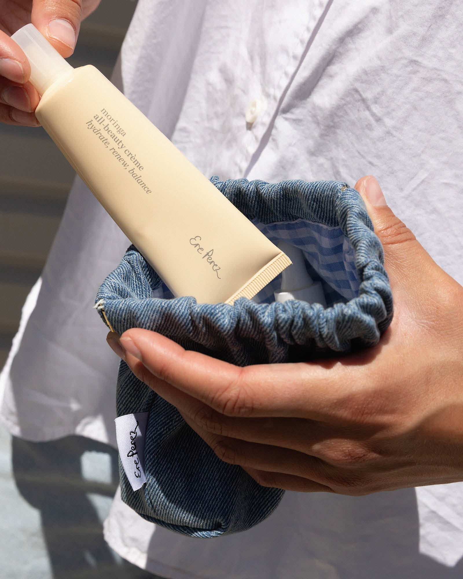Person holding a bottle of moringa face cream in a blue pouch.