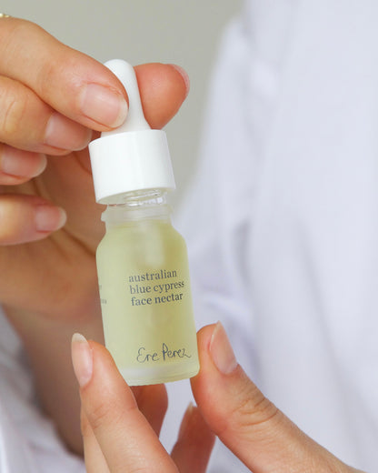 A hand holding a small glass dropper bottle of Eke Aroa Australian Blue Cypress Face Nectar against a soft white background 