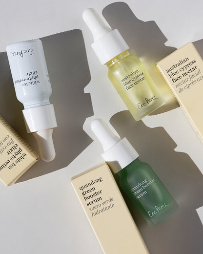 Four skincare dropper bottles and matching cream-colored product boxes arranged on a light gray surface with soft shadows 