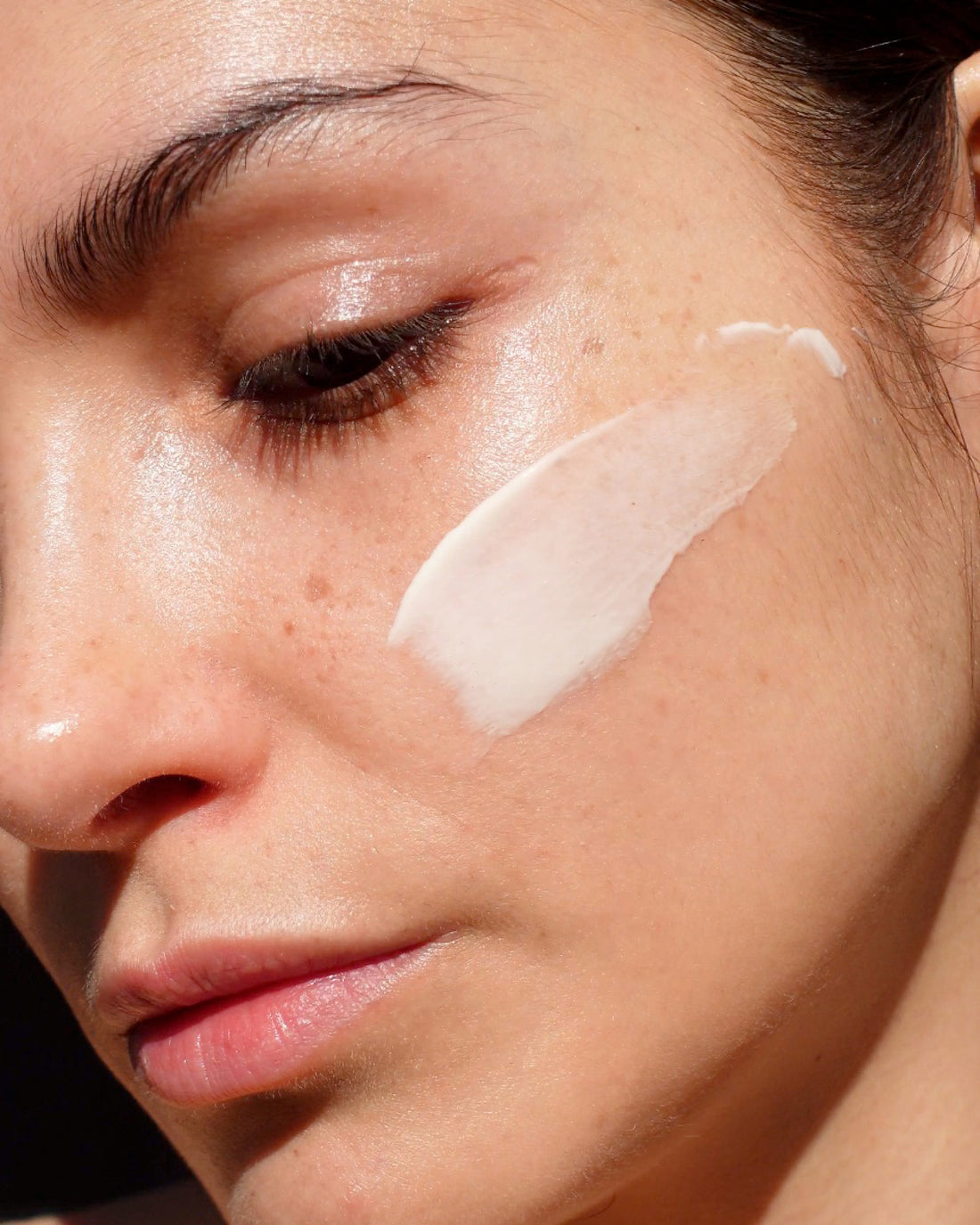 Close-up of a woman's face with a white cosmetic product applied to her cheek.