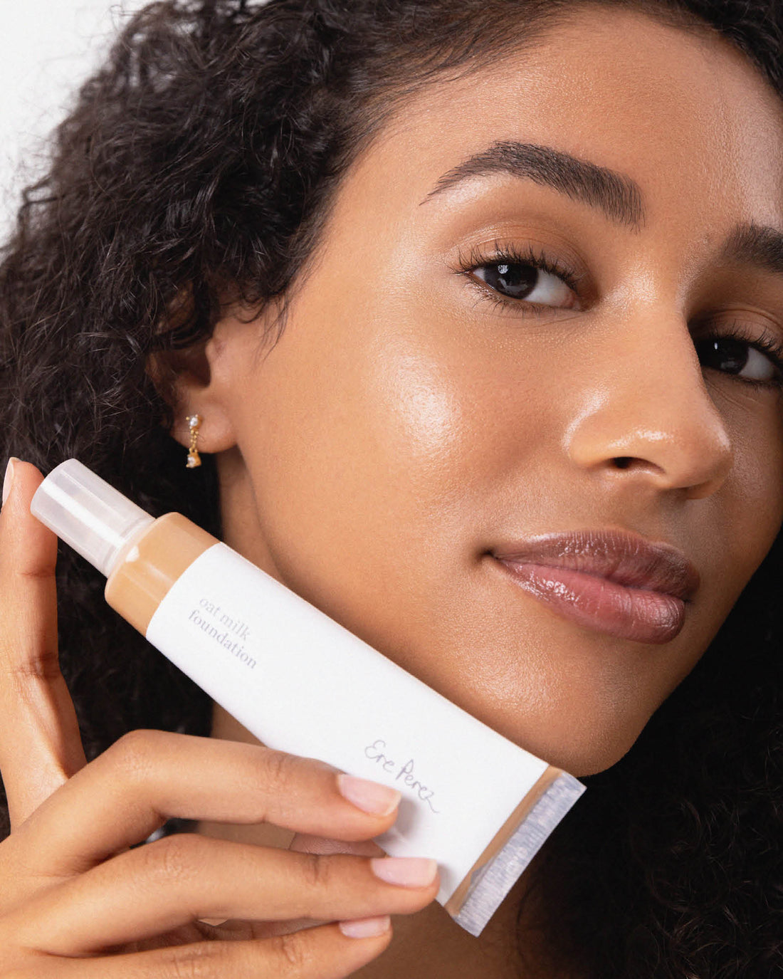 Woman holding a cosmetic tube close to her face. Oat Milk Foundation in Pecan, #shade_pecan